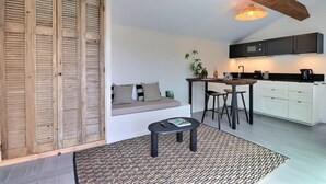 Une cuisine moderne équipée d’un four à micro-ondes encastré, un coin repas avec une table et des chaises, et un espace détente avec un canapé et des coussins.