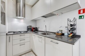 Une cuisine moderne avec des meubles blancs, des appareils en acier inoxydable et un plan de travail noir.