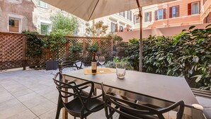 Une terrasse extérieure avec une table et des chaises, une bouteille de vin et des verres.