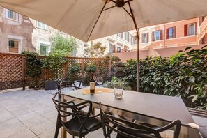 Une terrasse extérieure avec une table et des chaises, une bouteille de vin et des verres.