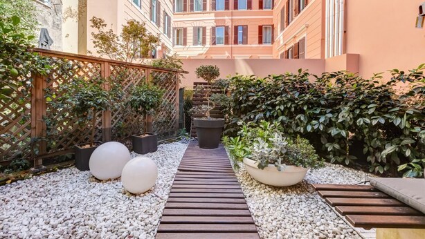 A courtyard with a wooden pathway, potted plants, and a small tree. - Cozy Studio with private Outdoor Space - FromHometoRome (Roma)