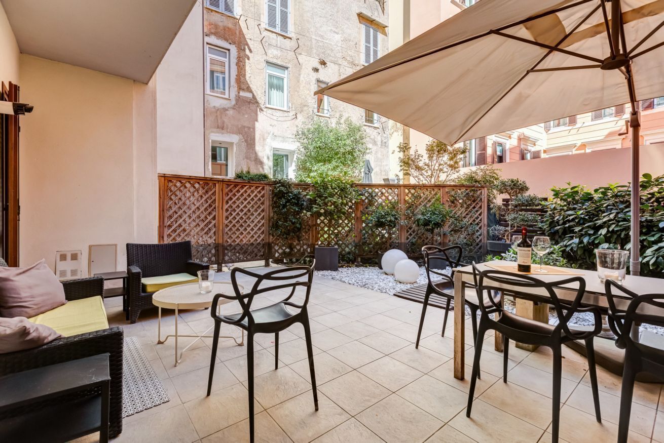 Ein Patio mit Gartenmöbeln, darunter Stühle und ein Tisch, umgeben von einem Holzzaun und Pflanzen.