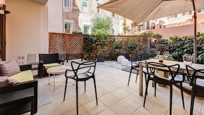 Un espace patio aménagé avec du mobilier d’extérieur, notamment des chaises et une table, entouré d’une clôture en bois et de plantes.