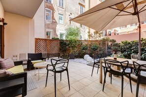 Un espace patio aménagé avec du mobilier d’extérieur, notamment des chaises et une table, entouré d’une clôture en bois et de plantes.