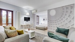 Un salon moderne avec un canapé, une table basse et un téléviseur. Il y a également un coin repas avec des chaises et une table. La pièce est dotée d’une grande fenêtre et d’un mur orné d’un motif circulaire.