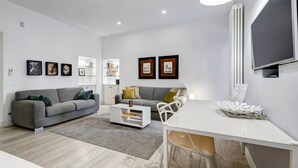 A modern living room with a grey sofa, a white coffee table, and a dining area with a white table and chairs. - Cozy Studio with private Outdoor Space - FromHometoRome (Roma)