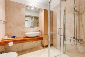 Une salle de bain moderne avec un grand miroir, un lavabo sur colonne et une douche à parois de verre.
