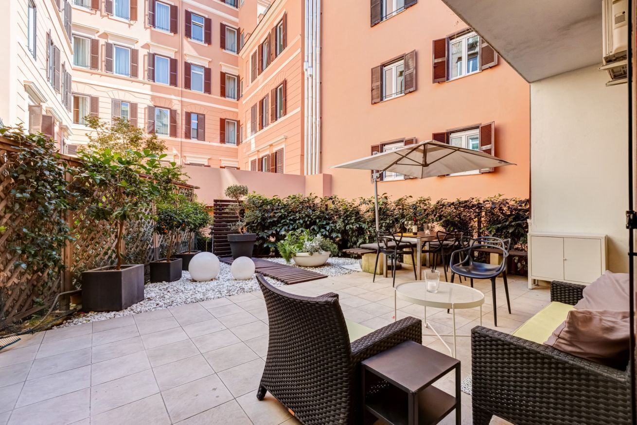 A courtyard with outdoor seating, potted plants, and a building with multiple windows.