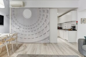 A modern kitchen with white cabinets, a built-in oven, and a dining area with a white table and chairs.