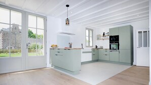 A modern kitchen with light green cabinets, a white countertop, and a large window providing a view of the outside.
