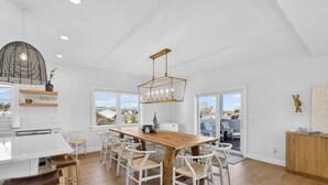 Una cocina amplia con una mesa y sillas de madera, una lámpara colgante y ventanas grandes que ofrecen vistas al exterior.