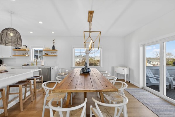 A modern kitchen with a wooden dining table, white chairs, and a large window offering a view of the outdoors.