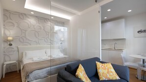 A modern bedroom with a bed, a sofa, a small table, and a kitchenette. - WePuglia – Appartamento Grottelle (Polignano a Mare)