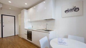A modern kitchen with white cabinets, a sink, and a dining area with a table and chairs. - WePuglia – Appartamento Grottelle (Polignano a Mare)