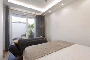 Quarto de hotel moderno com cama, área de estar, uma mesinha e vista através de uma porta de vidro.