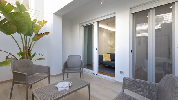 A balcony with wicker furniture, a potted plant, and a sliding glass door leading to a living area. - WePuglia – Appartamento Grottelle (Polignano a Mare)