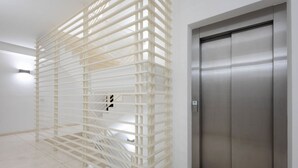 A modern elevator with a metallic finish, a white wall, and a white, grid-like structure in the foreground. - WePuglia – Appartamento Grottelle (Polignano a Mare)