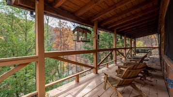 A wooden deck with benches and a birdhouse, overlooking a forested area.
