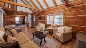 A spacious log cabin interior with a high ceiling, wooden beams, a cozy living area with sofas and a coffee table, and a dining area with a table and chairs. - Cabin in the Trees, Hot Tub, Fire Pit (Rockbridge)
