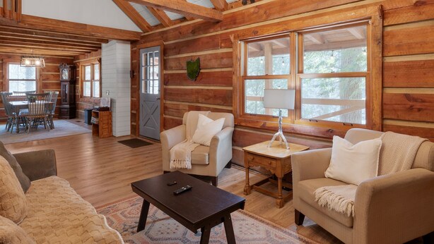 A spacious log cabin interior with a high ceiling, wooden beams, and a cozy seating area with sofas and a coffee table. - Cabin in the Trees, Hot Tub, Fire Pit (Rockbridge)
