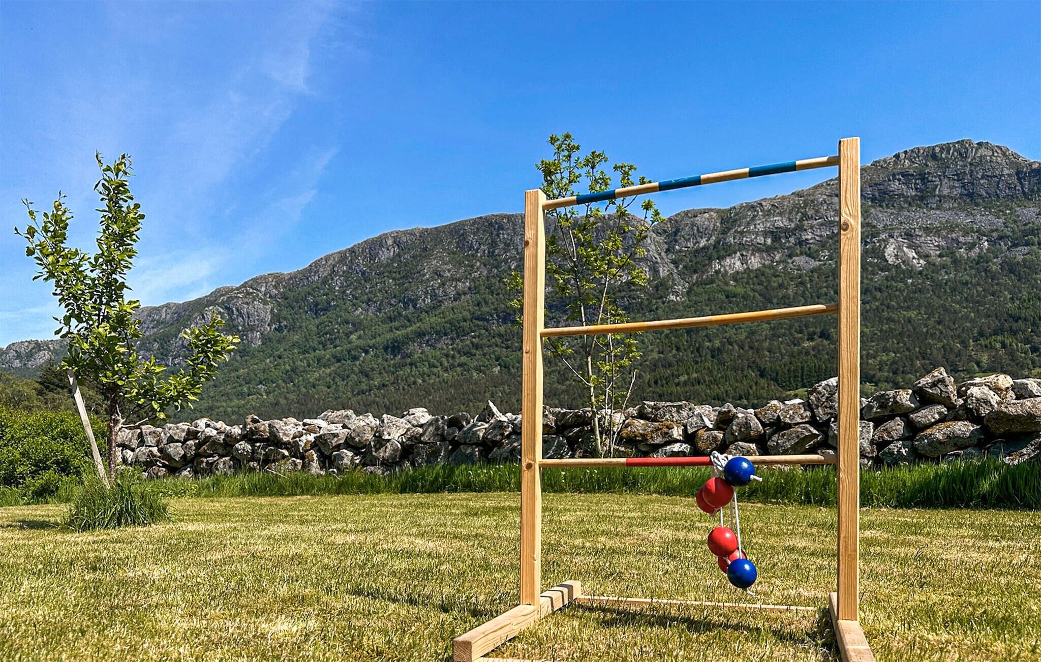 Un ensemble de balançoires en bois installé dans un champ herbeux, avec un mur de pierres et des montagnes en arrière-plan.