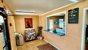 A hotel reception area with a check-in counter, a refrigerator, a vending machine, a plant, and a welcome sign. - Seagoville Inn (Seagoville)