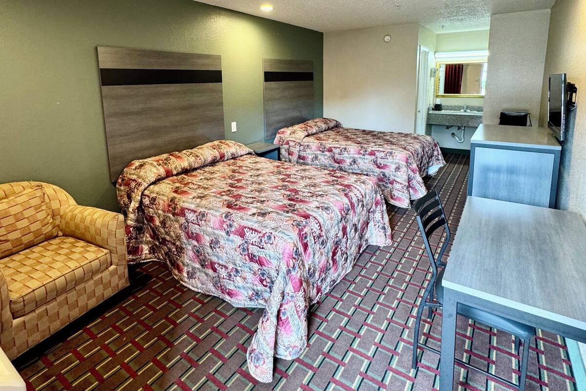 A hotel room with two beds, a sofa, a table, and a kitchenette.