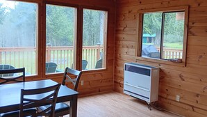 Una cabaña de madera con una mesa y sillas para comer, ventanas amplias y un equipo de aire acondicionado.