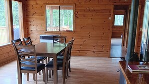Interior de una cabaña de madera con comedor, un ventanal grande y chimenea.