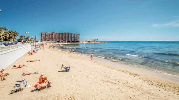 A beach with a large hotel in the background, sandy beach, and clear blue sky. - 2 bedroom stunning apartment in Torrevieja (Torrevieja)