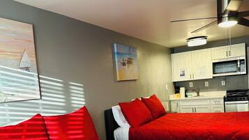 A bedroom with two beds, a ceiling fan, a painting, and a kitchenette.