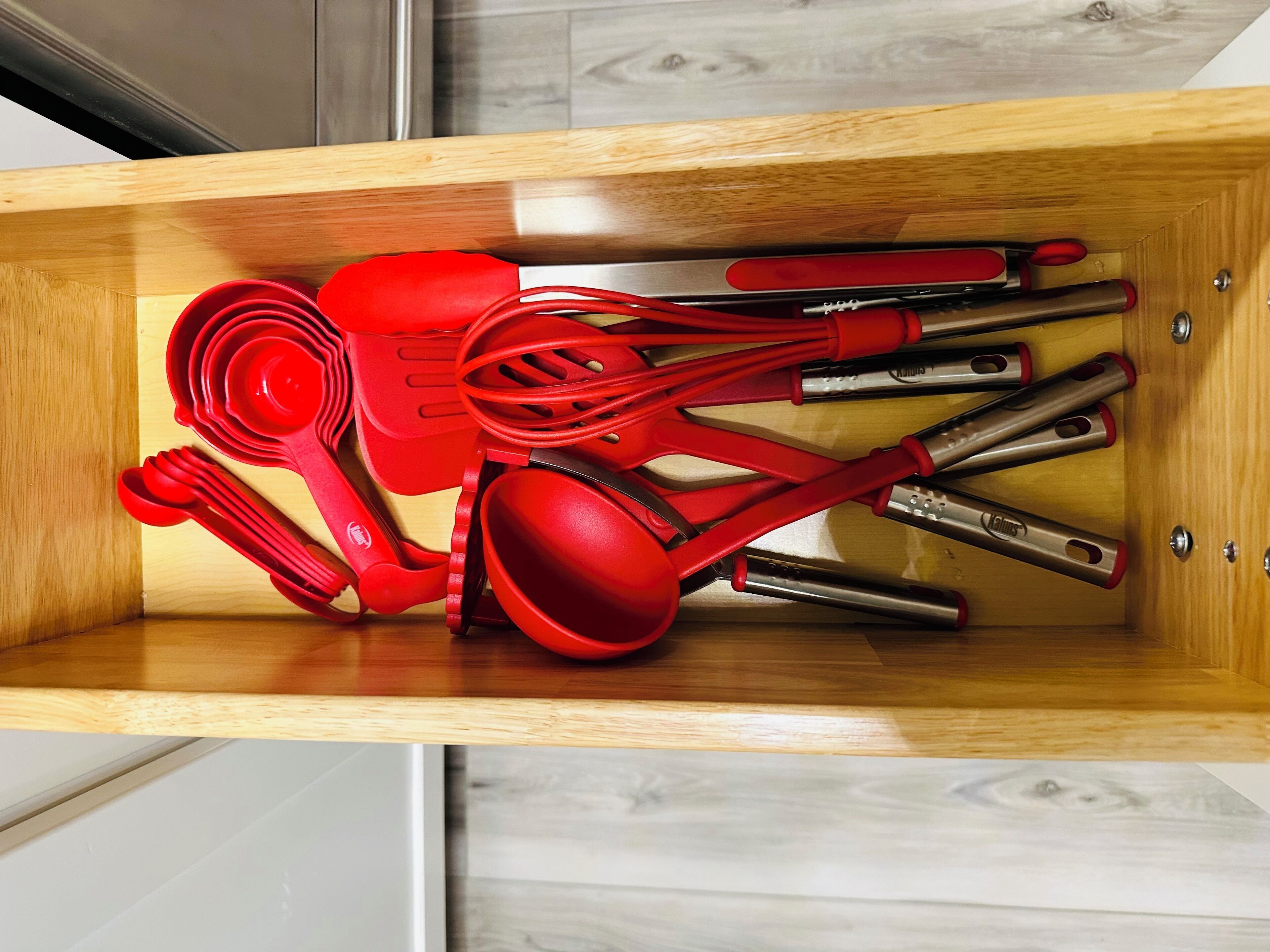 A drawer containing red kitchen utensils including a ladle, spatula, and measuring spoons.