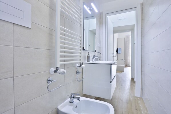 A modern bathroom with a sink, mirror, towel rack, and a shower area.