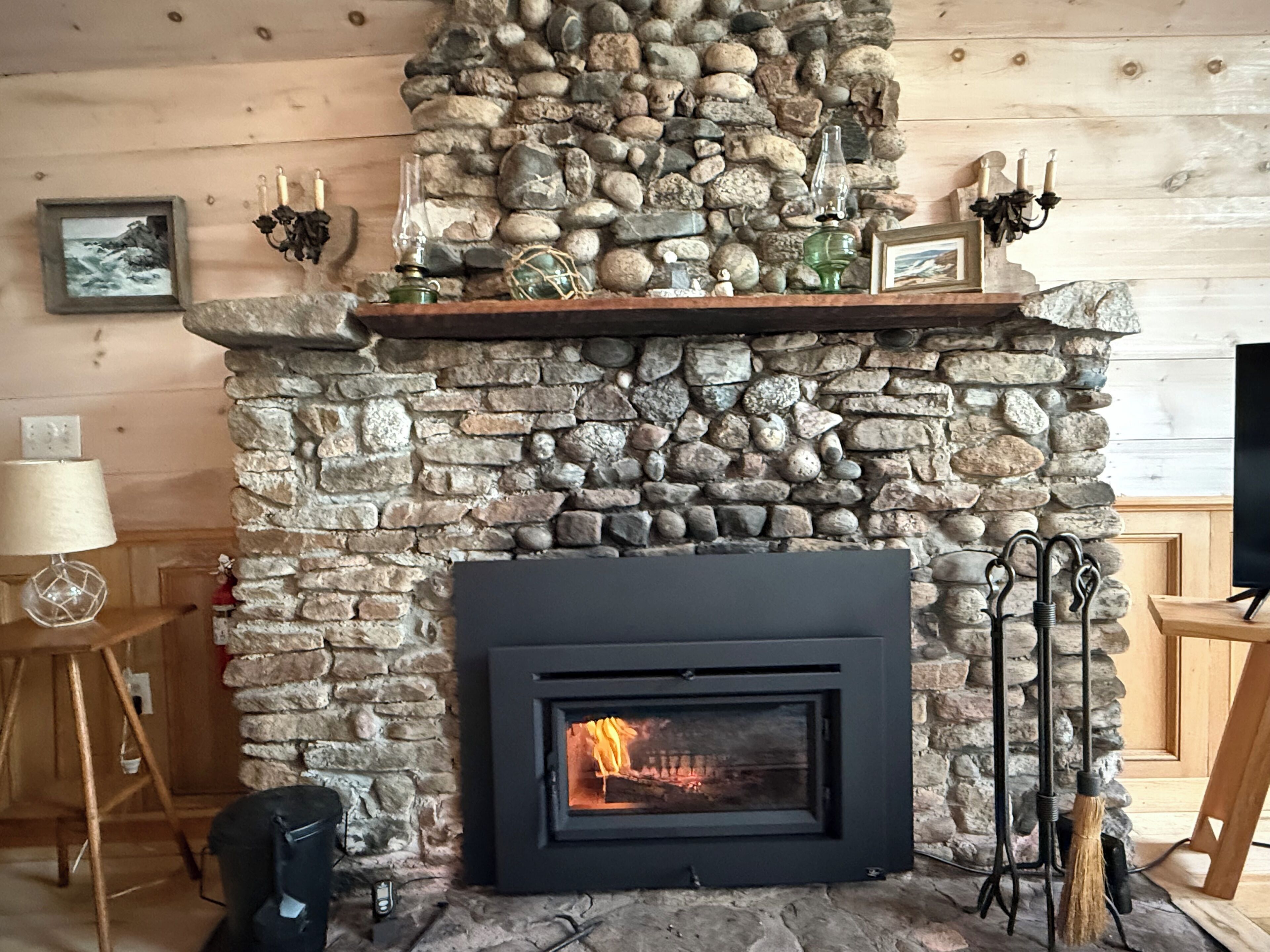 A stone fireplace with a black front, surrounded by a wooden wall and a shelf with decorative items.