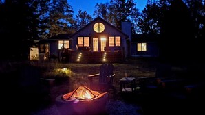 A cabin with a circular window design, a fire pit, and a well-lit exterior.