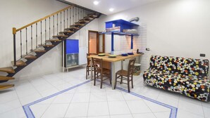 Ein kompakter Wohnraum mit Treppe, einer Küchenzeile, einem Essbereich und einer Couch.