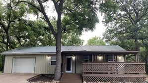 A single-story building with a garage, a front door, and a small porch with a lattice railing. - Little Sac Lake House w Starlink internet (Greenfield)