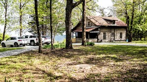 A rustic cabin with a wooden exterior and a metal roof, surrounded by trees and parked vehicles.