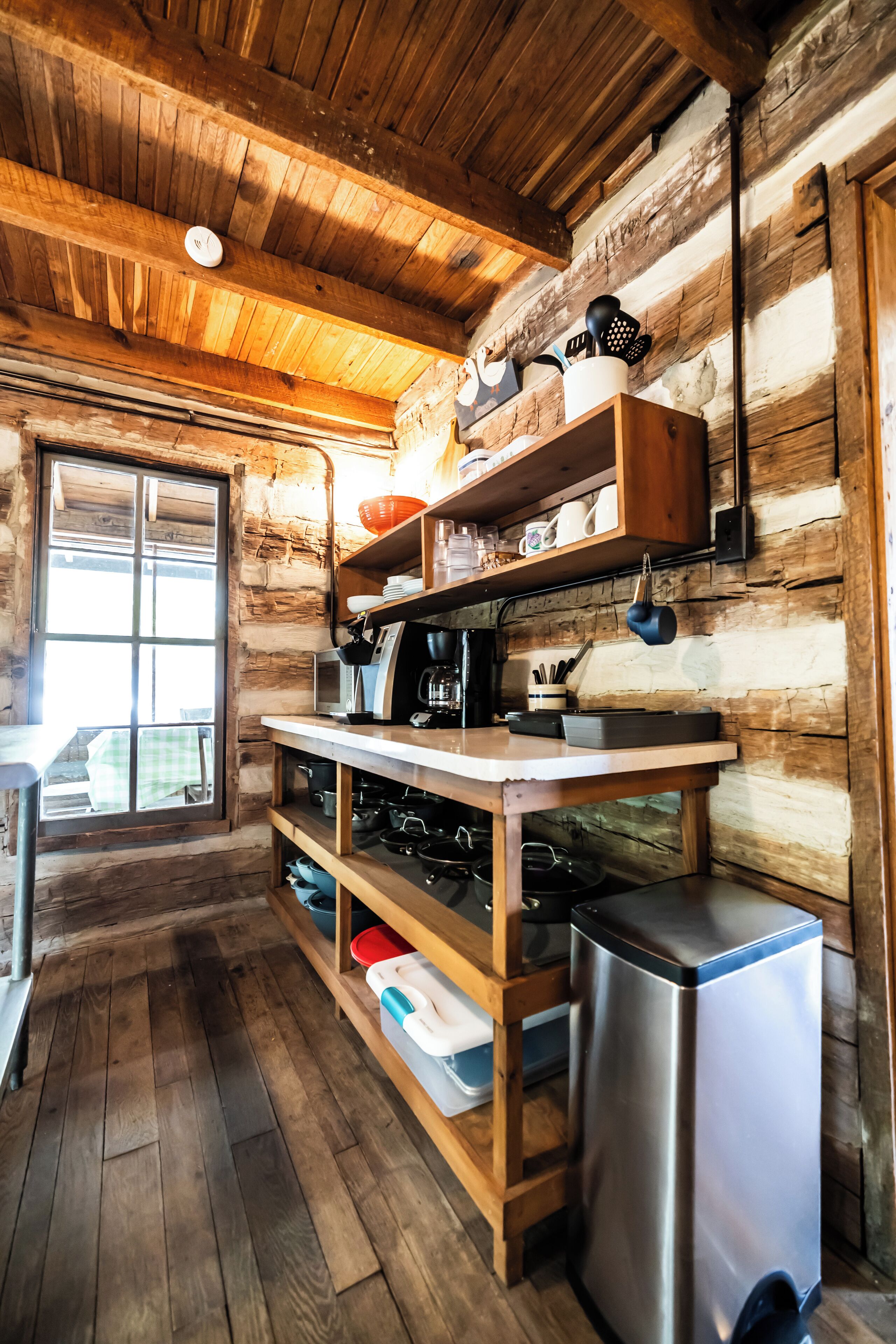 Une cuisine rustique aménagée dans une cabane en bois, avec un plafond en bois, une fenêtre et un réfrigérateur en acier inoxydable.
