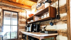 A rustic wooden cabin kitchen with a wooden ceiling, a window, and a stainless steel refrigerator.