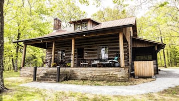 Une cabane rustique en rondins de bois, dotée d’un porche, de fondations en pierre et d’une cheminée.