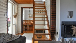 A staircase leading to a dining area with a wooden table and chairs, a fireplace, and a view of a red barn outside.