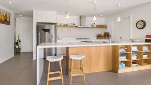 A modern kitchen with white cabinetry, a central island with stools, pendant lighting, and a clock on the wall. - Berry Beach Farm (Berry)