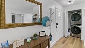 A laundry room with two stacked front-loading washers and dryers, a wooden vanity with a mirror, and a door leading to another room. - Gorgeous relaxing 2BD Near Ft. Myers Beach (Fort Myers)
