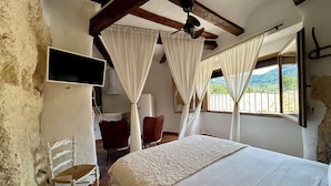 Quarto com cama, televisão, cadeira e janela com cortinas.
