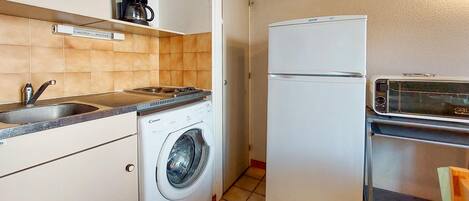 A compact kitchen with a washing machine, a refrigerator, a coffee maker, and a toaster.
