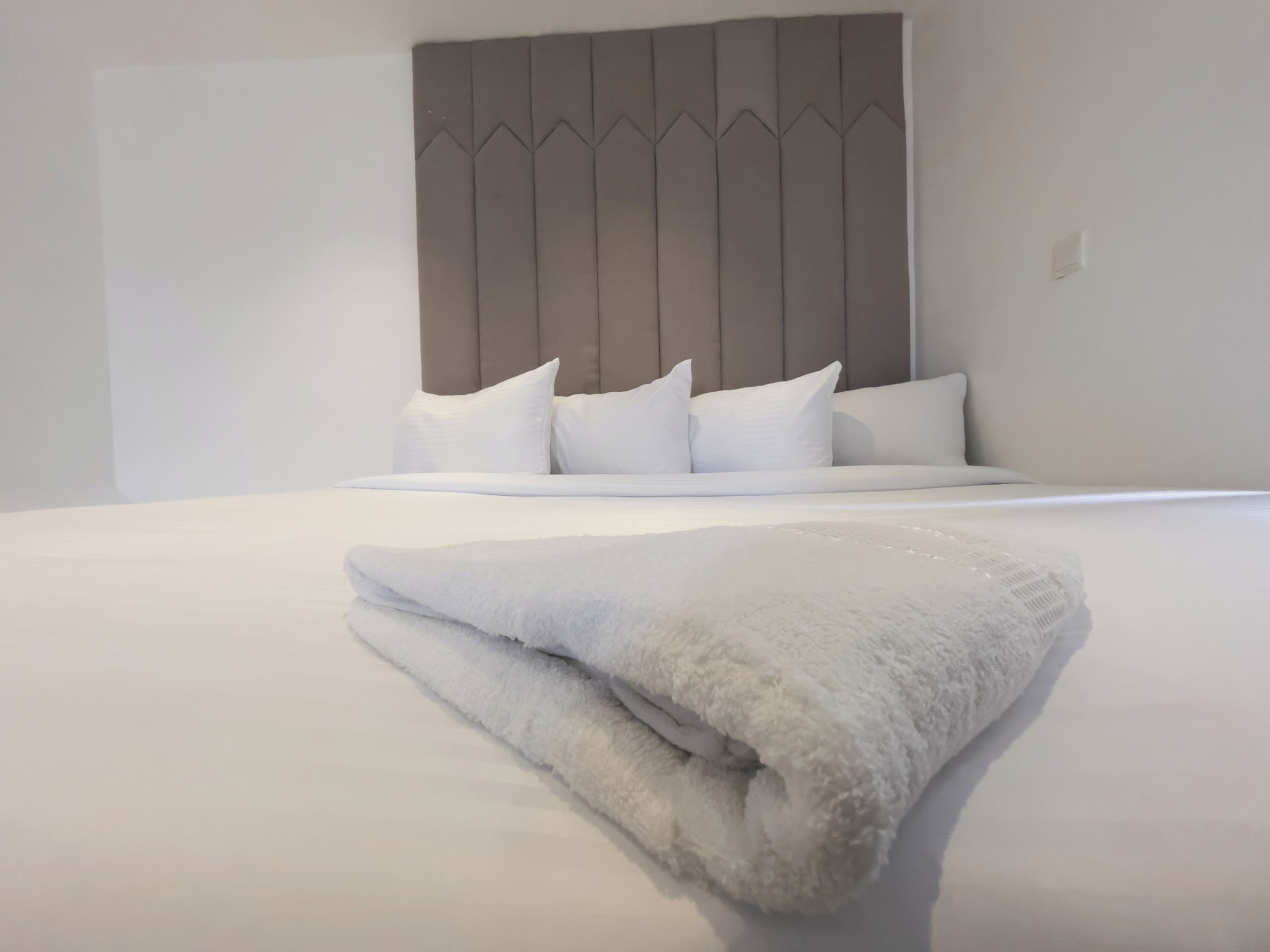 Una cama bien hecha con sábanas y almohadas blancas, un cabecero gris y una manta blanca doblada sobre la cama.