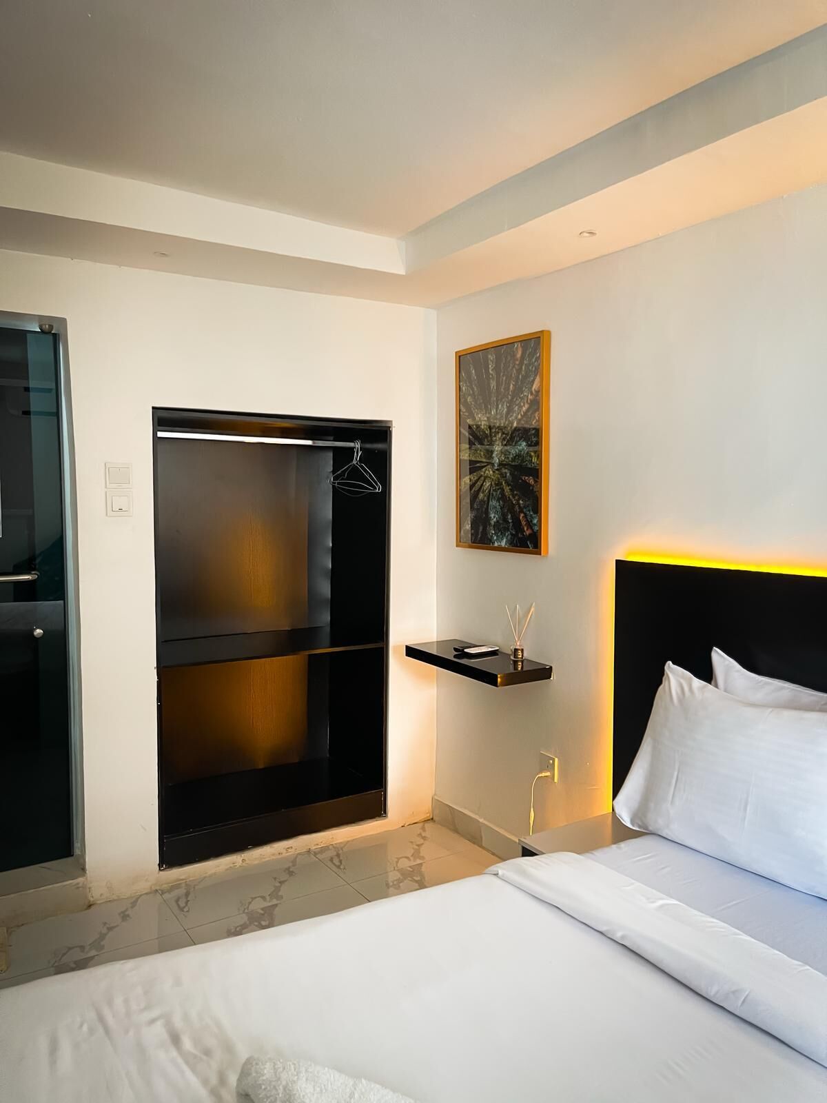 A hotel room with a bed, a built-in wardrobe, a bedside table with a lamp, and a framed artwork on the wall.