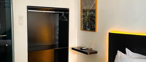 A hotel room with a bed, a built-in wardrobe, a bedside table with a lamp, and a framed artwork on the wall.