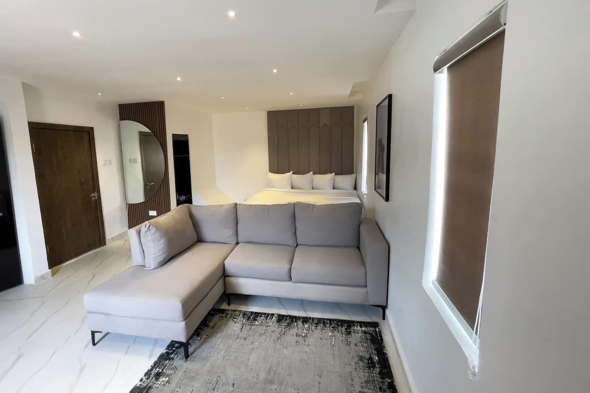 A modern hotel room with a large bed, a sofa, a wardrobe, and a mirror.